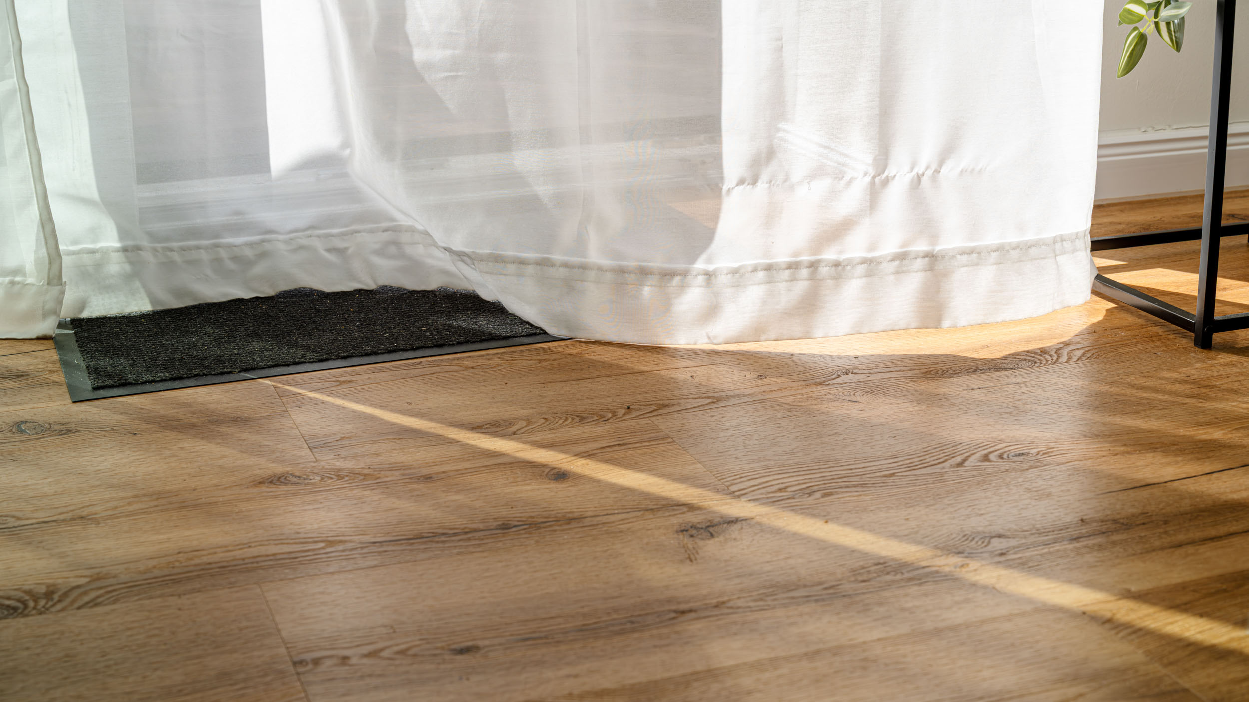 Junge Frau in Latzhose kniet auf dem Boden und hält lächelnd ein helles Laminatbrett in einem renovierungsbedürftigen Raum